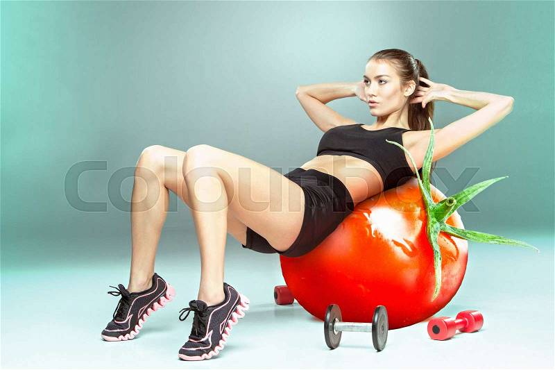 Sporty woman doing aerobic exercise on a tomato as fitness ball. Concept of diet and healthy foods and lifestile, stock photo