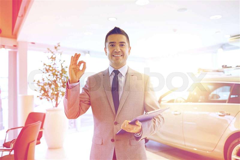 Auto business, car sale, consumerism, gesture and people concept - happy man with clipboard showing thumbs up at auto show or salon, stock photo