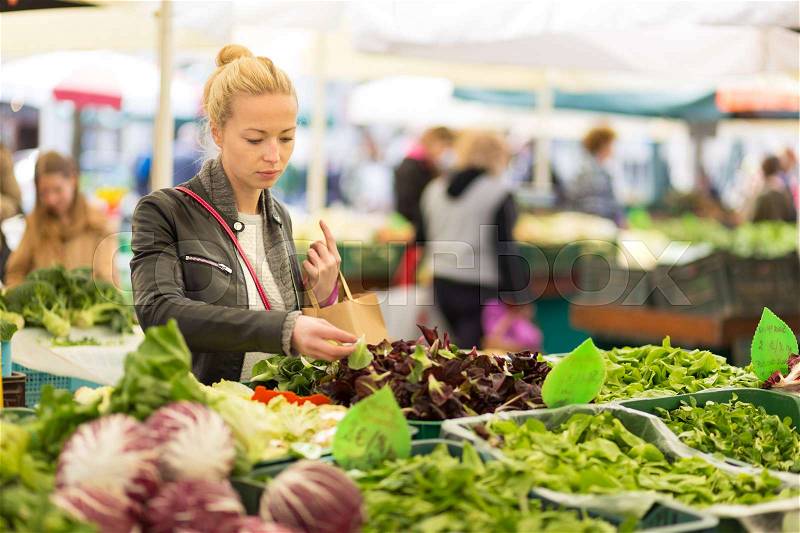Woman buying fruits and vegetables at local food market. Market stall with variety of organic vegetable, stock photo