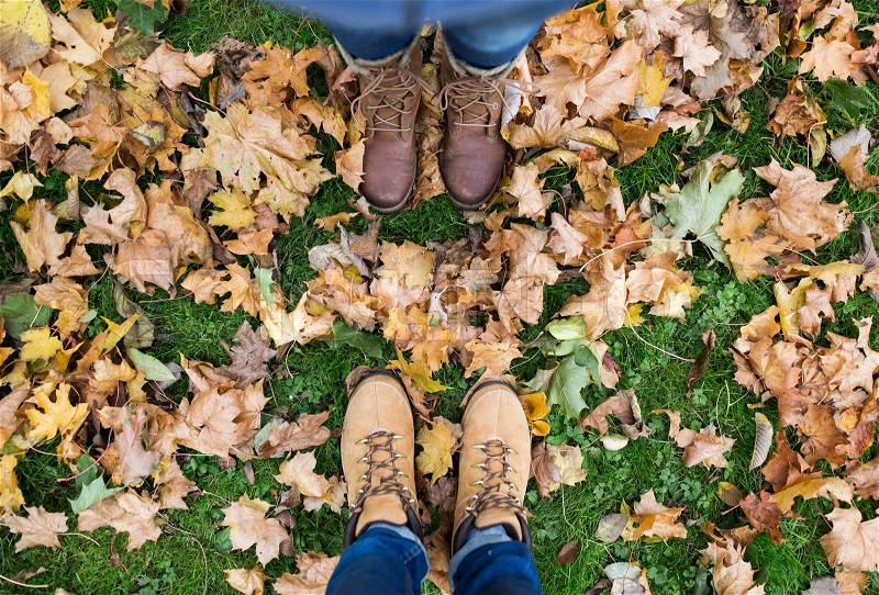 Season and people concept - couple of feet in boots with autumn leaves on ground, stock photo