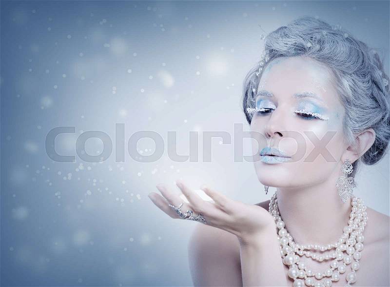 Winter Woman Fashion Model Blowing Snow at Night. Snow Queen Girl on Blue Background with Stars, Snow and Glitters, stock photo