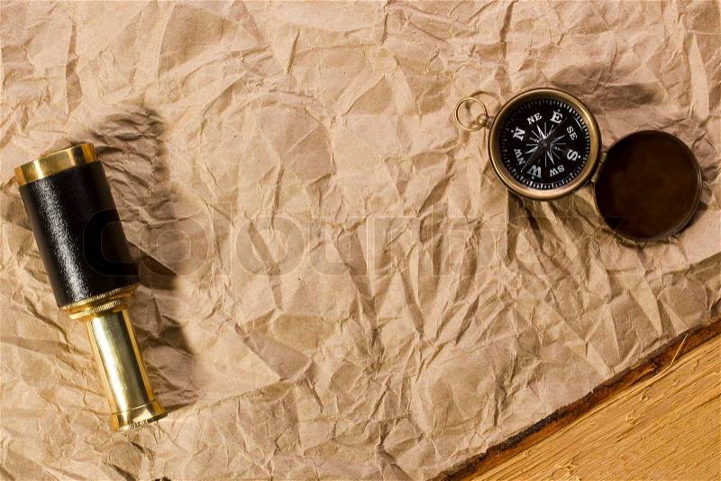 A golden compass and a spyglass laying on an old wrinkled brown paper that can serve as a background for a message or a drawing of a map, stock photo