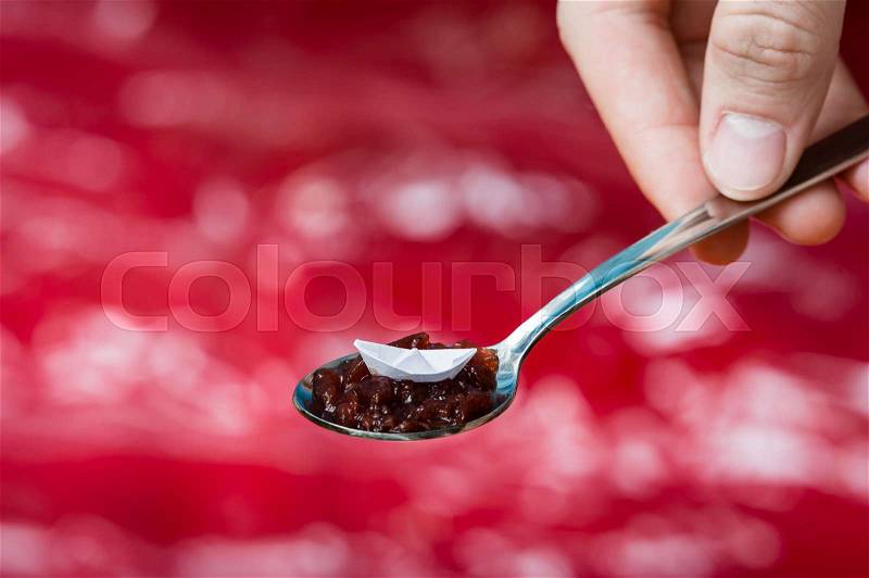 Hand holding spoon with very small paper boat. Origami ship over the red ocean, stock photo