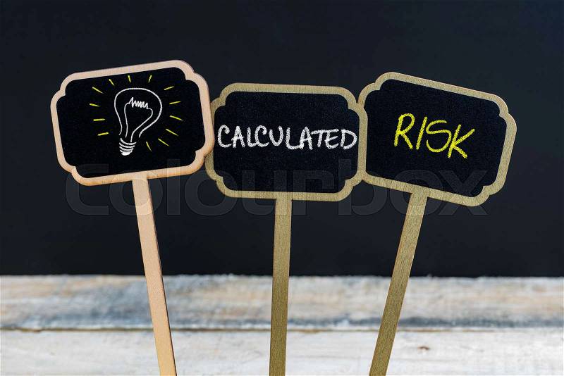 Concept message CALCULATED RISK and light bulb as symbol for idea written with chalk on wooden mini blackboard labels, defocused chalkboard and wood table in background, stock photo