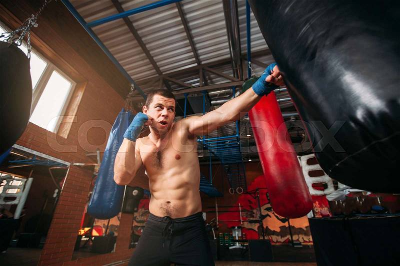 Strength male boxer training with punching bag. Boxing exercise. Sport gym on the background, stock photo
