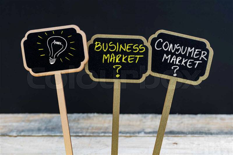 Concept message BUSINESS MARKET versus CONSUMER MARKET and light bulb as symbol for idea written with chalk on wooden mini blackboard labels, defocused chalkboard and wood table in background, stock photo