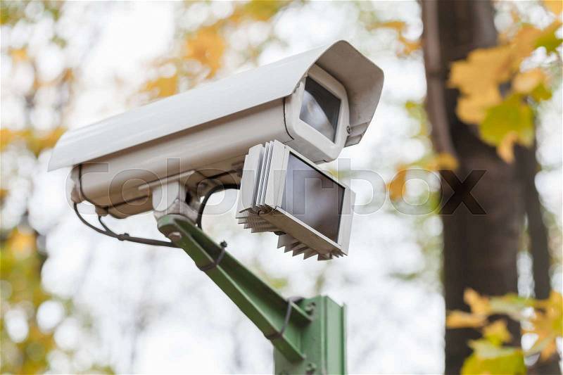 Close-up photo of an outdoor surveillance camera with motion detector in autumnal park, stock photo
