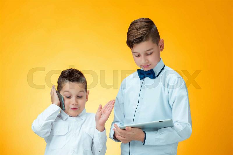 The two little boys using laptop and mobile phone on orange background, stock photo