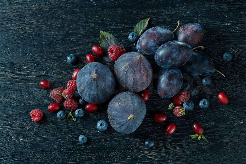 Ripe figs and berries with a bunch of basil on the wooden black background, stock photo