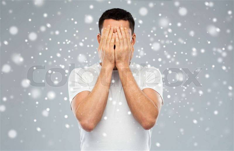 People, fear, emotions, winter and stress concept - man in white t-shirt covering his face with hands over snow on gray background, stock photo