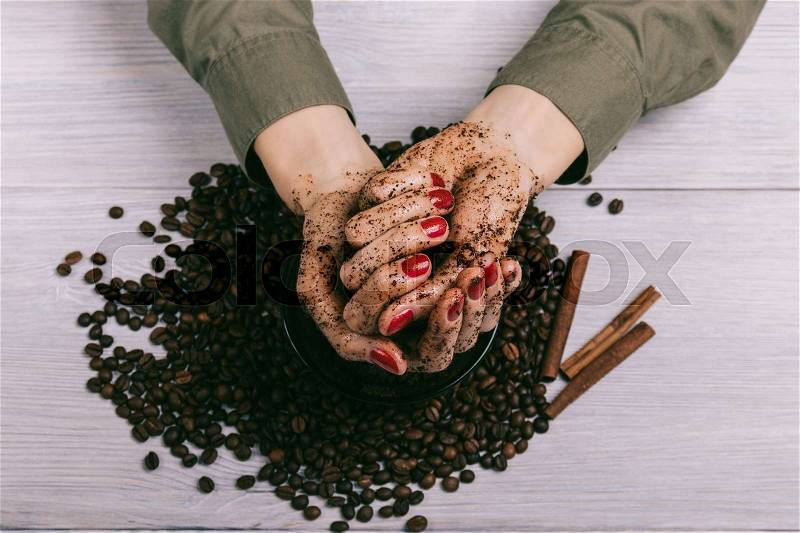 Female hands with red manicure with applied scrub over coffee beans, close-up, stock photo