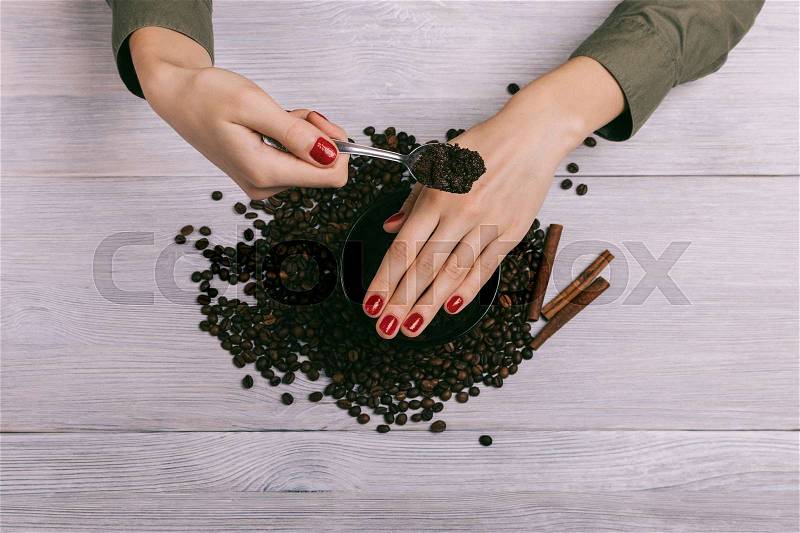Woman applies coffee scrub on hands with a red manicure, stock photo