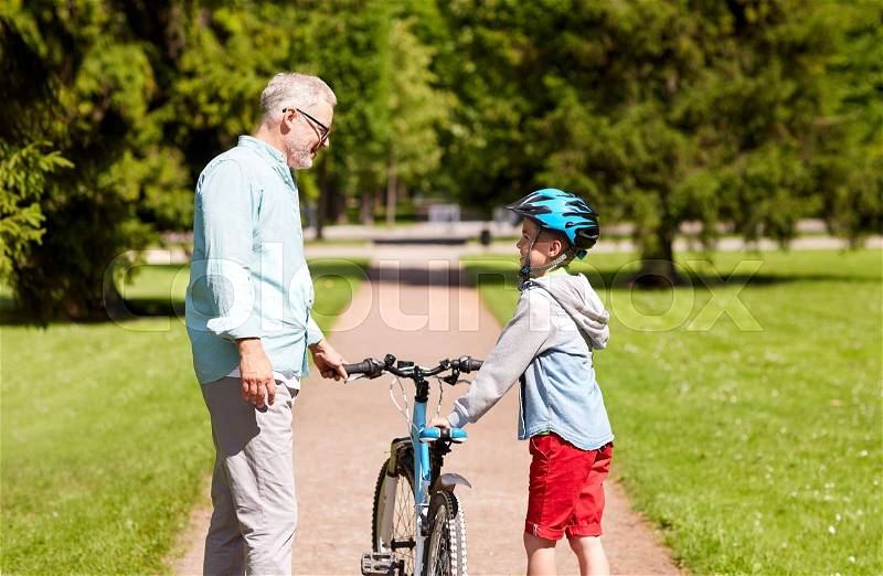 Family, generation, safety and people concept - happy grandfather and boy with bicycle and bike helmet talking at summer park, stock photo