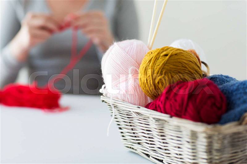 People and needlework concept - wicker basket with knitting needles and balls of yarn over woman, stock photo