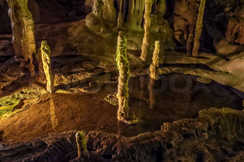 Cave with colourful textured walls and stalactites and stalagmite in the puddle, stock photo