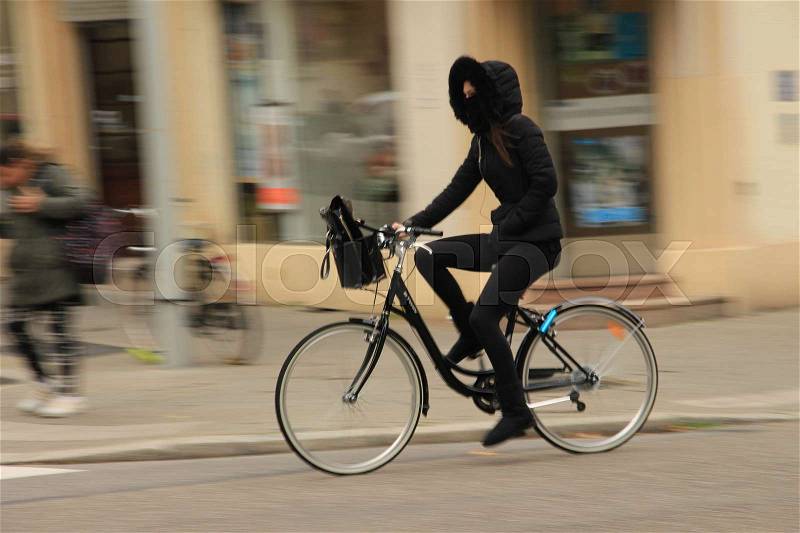 The lady on the bike is covered her face with a black shawl against the extremely cold in the city in winter time, stock photo