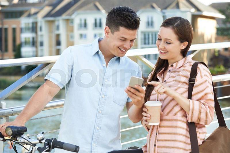 Young Couple Looking At Phone On Way To Work In Urban Setting, stock photo