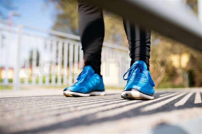 Legs of unrecognizable runner standing on concrete path wearing blue sports shoes, close up, stock photo