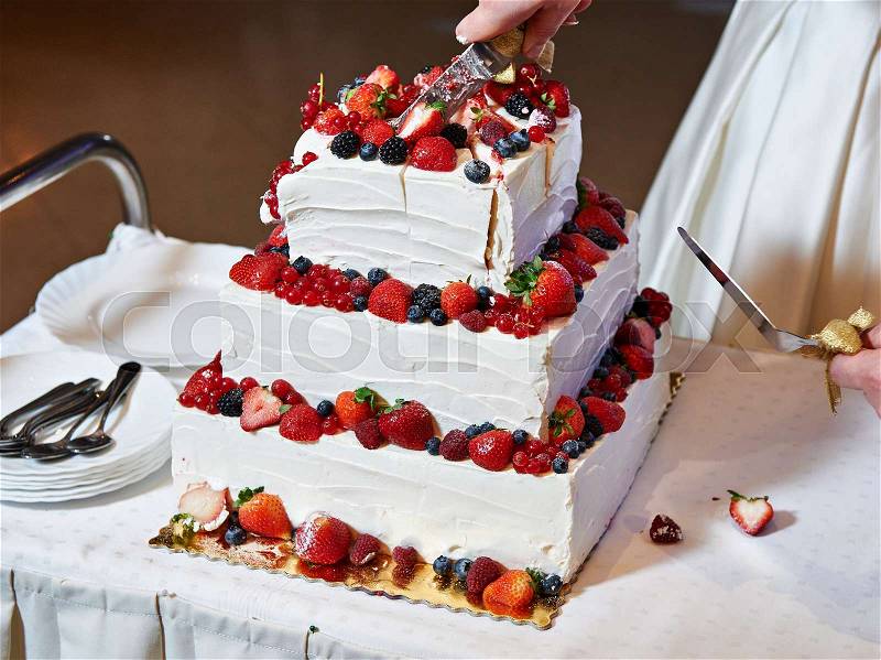 Cutting the wedding cake with berries on banquet, stock photo