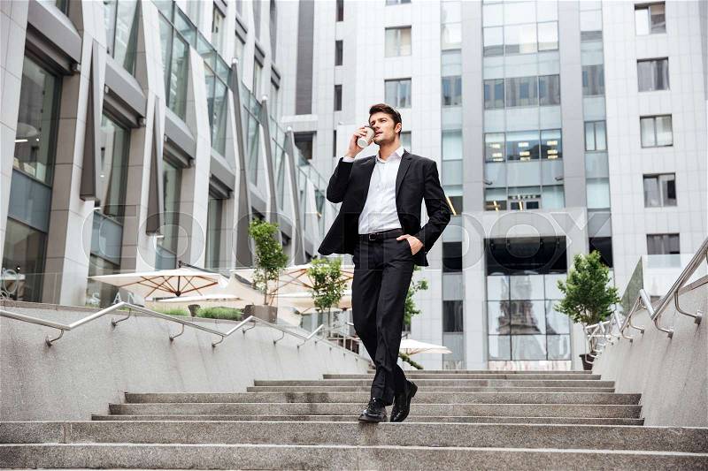 Attractive young businessman walking and drinking take away coffee in the city, stock photo