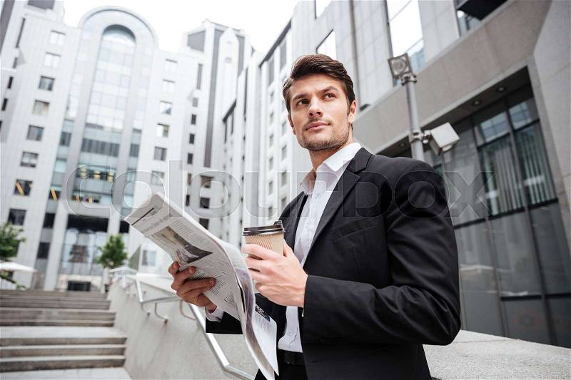 Handsome young businessman reading newspaper and drinking coffee in the city, stock photo