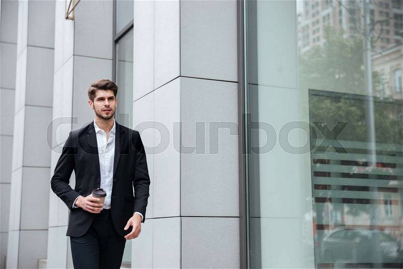 Serious young businessman walking and drinking take away coffee in the city, stock photo