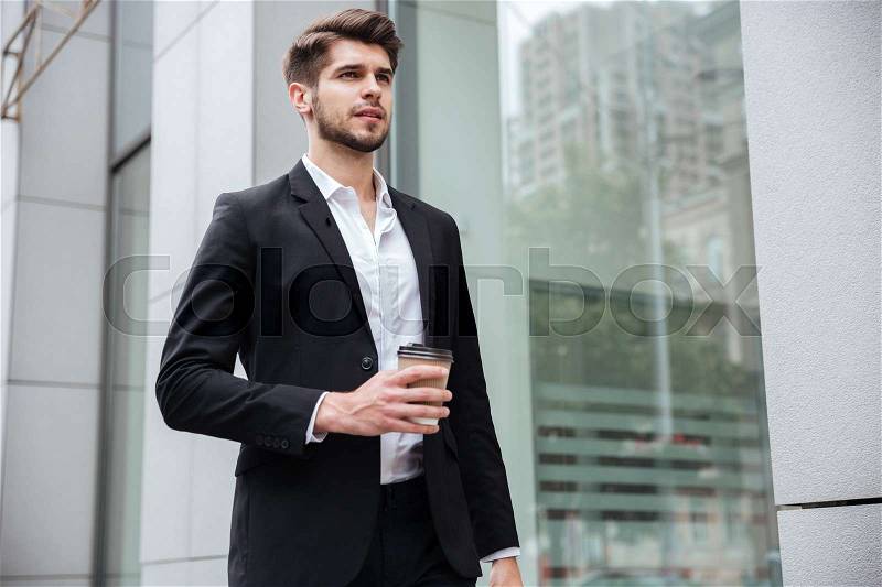 Confident young businessman walking and drinking coffee outdoors, stock photo
