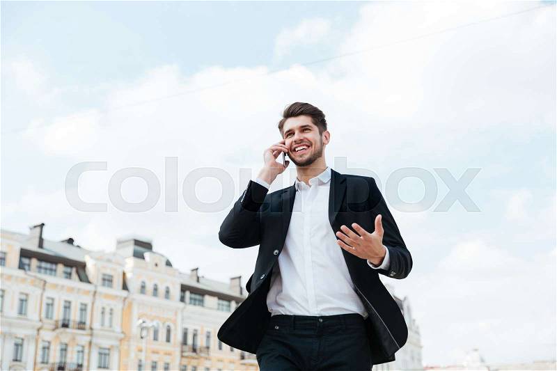 Cheerful attractive young businessman standing on the street and talking on cell phone, stock photo