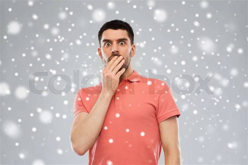Emotion, fear, winter, christmas and people concept - scared man in polo t-shirt over snow on gray background, stock photo