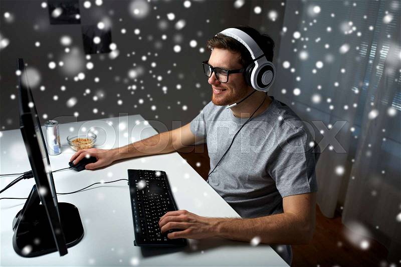 Technology, gaming, entertainment, let\'s play and people concept - happy young man in headset and glasses with pc computer playing game at home and streaming playthrough or walkthrough video over snow, stock photo