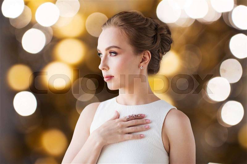 Jewelry, luxury, wedding, holidays and people concept - beautiful woman in white dress with diamond ring and earring over lights background, stock photo