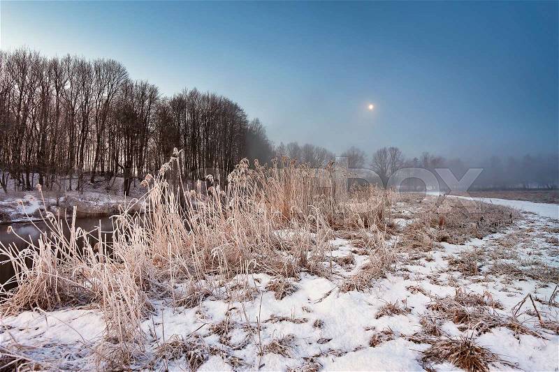 Moonlight in the winter dawn. Fog and mist on snowy winter river in Belarus, stock photo