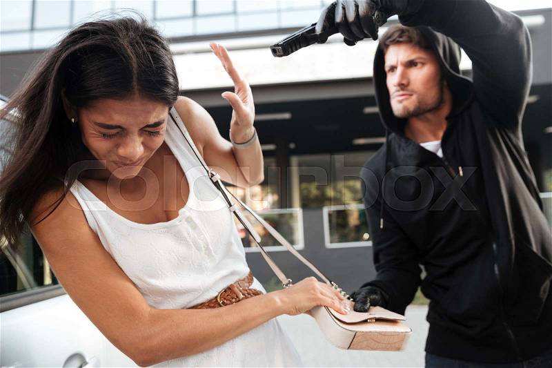 Aggressive young man with gun trying to steal purse of frightened young lady on the street, stock photo