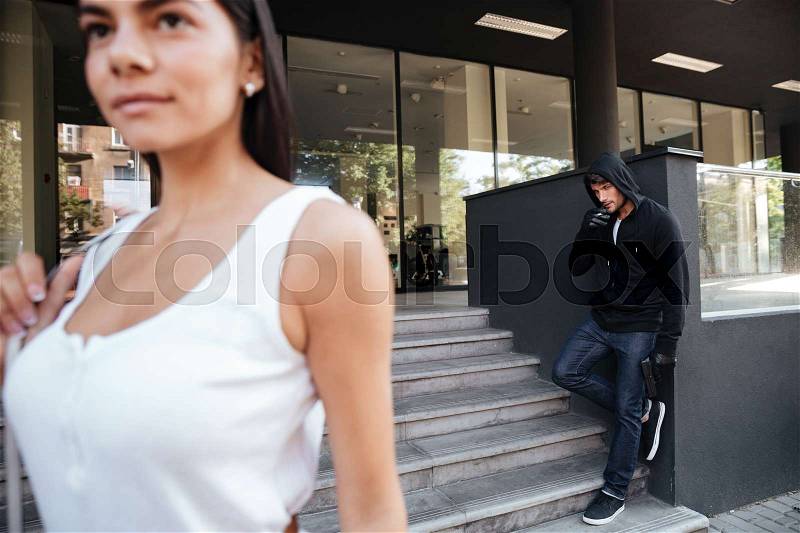 Criminal young man with gun smoking and looking for victim on the street, stock photo
