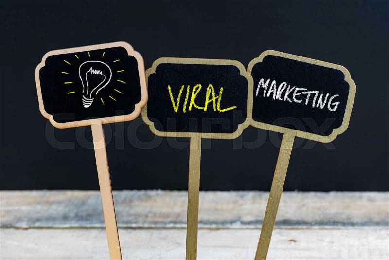 Concept message VIRAL MARKETING and light bulb as symbol for idea written with chalk on wooden mini blackboard labels, defocused chalkboard and wood table in background, stock photo