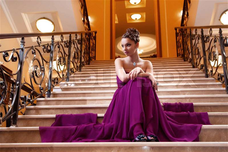 Woman in a long dress is sitting on the stairs in the hotel lobby, stock photo