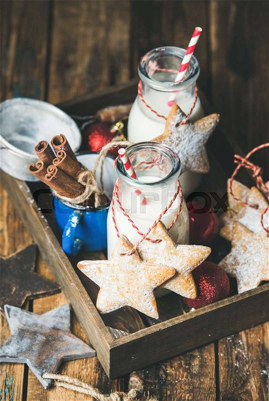 Christmas gingerbread star shaper cookies or bisquits with ropes and milk in bottles for Santa in wooden tray over rustic wooden background, selective focus, stock photo