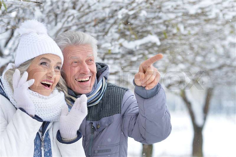 Portrait of exited senior couple having fun in winter park, man pointing at something, stock photo