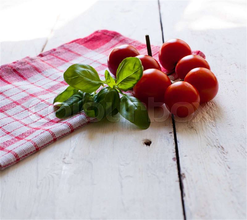 Ripe red cherry tomatoes on the napkin and fresh basil on the white old wooden table, stock photo