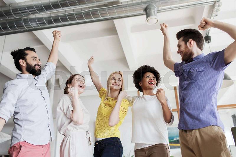 Business, triumph, gesture, people and teamwork concept - happy creative team raising hands up and celebrating victory in office, stock photo