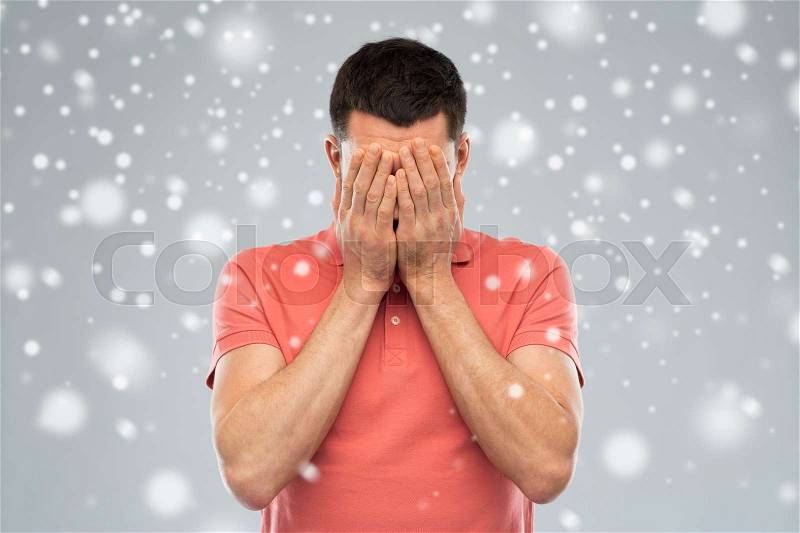 People, fear, emotions, winter and stress concept - man in white t-shirt covering his face with hands over snow on gray background, stock photo