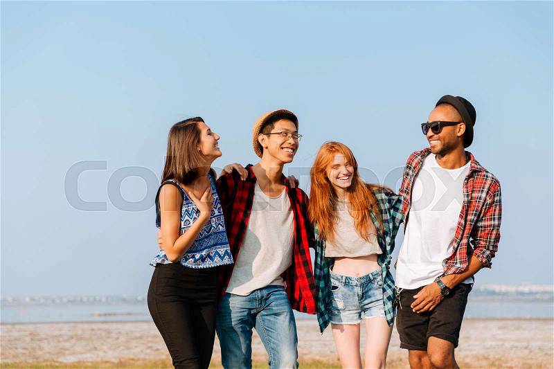 Multiethnic group of cheerful young friends standing together and laughing outdoors, stock photo
