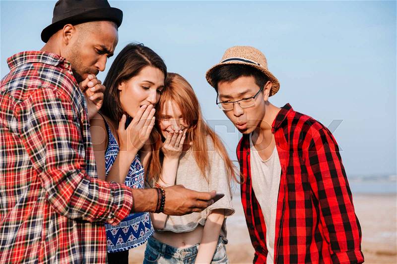 Group of amazed young people standing and looking at screen of cell phone together, stock photo