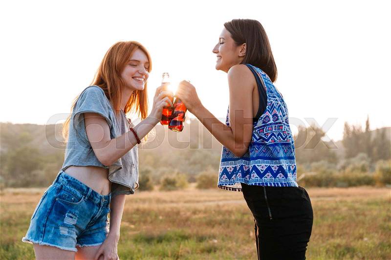 Two cheerful cute young women drinking soda and having fun outdoors, stock photo