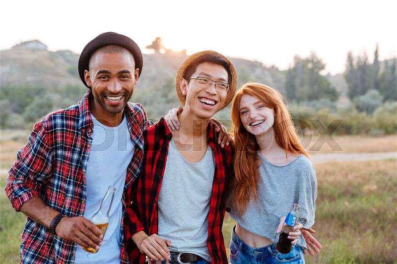 Portrait of smiling young people standing and hugging together outdoors, stock photo