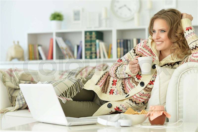 Young beautiful woman using laptop and drinking tea sitting on sofa at home, stock photo