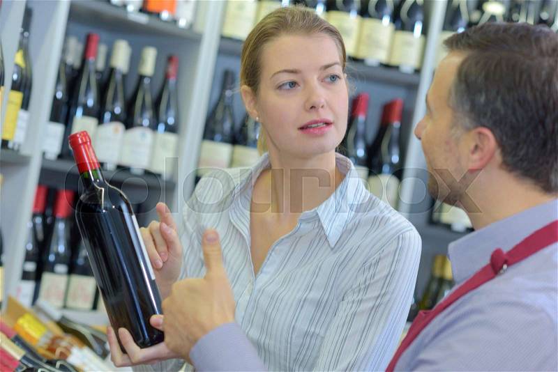 Sommelier giving woman recommendation for bottle of wine, stock photo