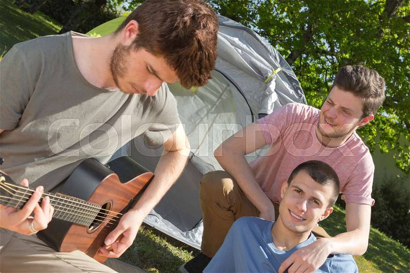 Friends camping and playing guitar, stock photo
