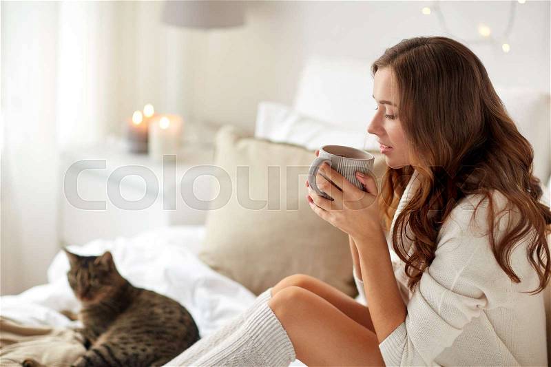 Morning, leisure, christmas, winter and people concept - happy young woman with cup of coffee or tea in bed at home bedroom, stock photo