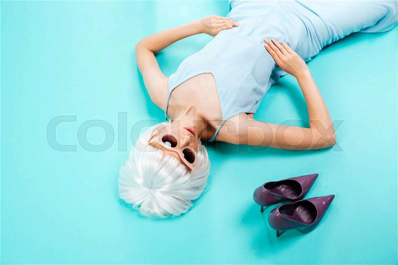 Top view of beautiful blonde young woman lying near her shoes over blue background, stock photo